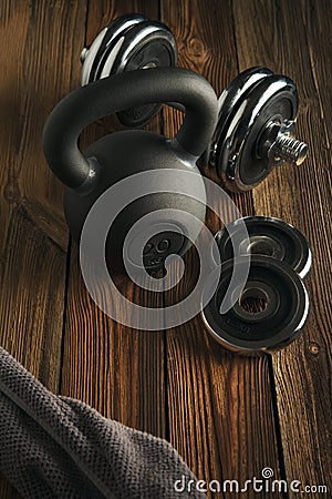 Top view of black iron kettlebell, dumbbell and grey towel on wooden floor Sport background with copyspace Stock Photo