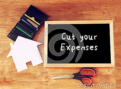 Top view of blackboard with the slogan cut your expenses scissors, wallet with credit cards and house shaped paper. household or Stock Photo