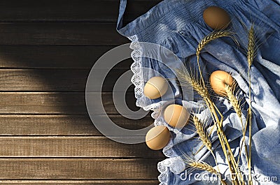 Top view of blue apron and eggs, golden wheat stems on it, wooden background.Empty space.Natural sun light Stock Photo