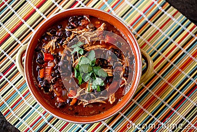 Top view of a bowl of homemade chilli topped with cilantro leaves on a colorful table mat Stock Photo