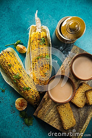 Top view of brewed hot milk tea with roasted grilled corn and fresh toast. Delicious Grilled Corncobs and Two Cups of Masala Chai. Stock Photo