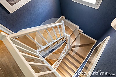 Top view of bright spiral staircase with polished wood parquet steps and matte white railings set against blue walls Stock Photo