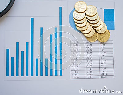 Top view of a bunch of coins over a paper full of graphics and charts, representing economy and finances Stock Photo