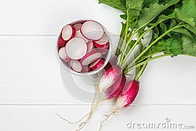 Top view of a bunch of radishes and a bowl of radish slices on a white wooden table Stock Photo