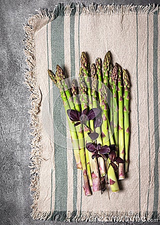 Top view of bundle of fresh green asparagus with purple basil leaves on a rustic line tablecloth. Stock Photo