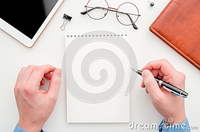 Top view businessman holding pen and taking notes at blank spiral notepad. Flat lay workspace with glasses, tablet and Stock Photo