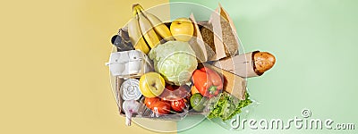 Top view of cardboard box with food products on color green-yellow background. Safe delivery. Banner with copy space Stock Photo