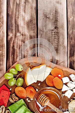 Top view of cheese plate - various types of cheese, honey, grapes, dried apricots, nuts and figs on a wooden board. Stock Photo