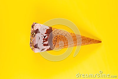 Chocolate flavor ice cream cone starts melting on yellow background Stock Photo