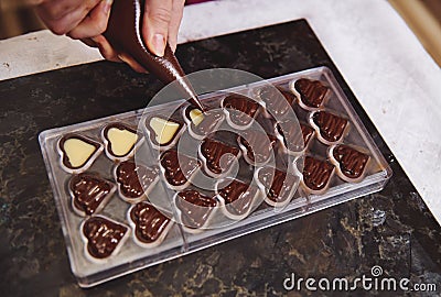 Top view of chocolatier squeezing filling of creamy liquid preparing luxury handmade chocolate pralines at home kitchen Stock Photo