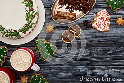 Top view of christmas pie, two cups of cocoa with marshmallows, spices and christmas tree cookies on dark wooden table. Stock Photo