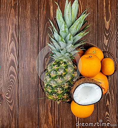 top view of citrus fruits as pineapple coconut orange tangerine in basket on wooden background with copy space Stock Photo