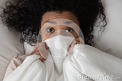 Young black woman peer out of white fluffy duvet Stock Photo
