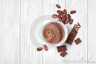 Top view of cocoa powder and beans with broken chocolate bar on white wooden background Stock Photo