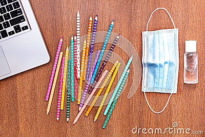 Top view of colored pencils with disinfectant gel, mask and a laptop detail on a wooden surface Stock Photo