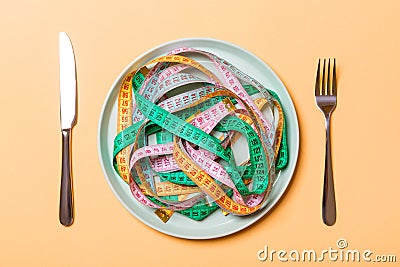 Top view of colorful measuring tapes on plate in the form of spaghetti with knife and fork on orange background. Weight loss and Stock Photo