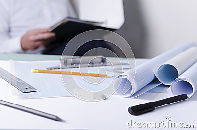 Draftsman at work, analyzing documents for drafting. Closeup of graph papers, rulers and other tools on the desk, engineer sitting Stock Photo