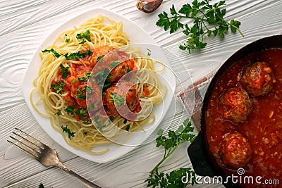 Top view cooked spaghetti in a plate and a pan with meatballs in tomato sauce on a white wooden background Stock Photo