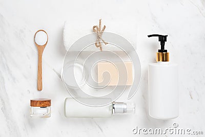 Top view of Cosmetic bottles, soap, wooden spoon and towel on white marble. Stock Photo