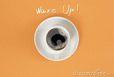 Top view of cup of black coffee and Wake Up lettering on orange background Stock Photo