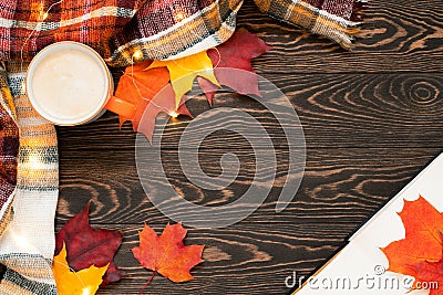 Top view of a cup of coffee, book, plaid scarf, fairy lights, yellow, orange and res leaves on the wooden table. Stock Photo