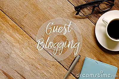 Top view of a cup of coffee eyeglasses,notebook and pen on wooden background written with GUEST BLOGGING Stock Photo