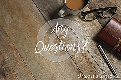 Top view of a cup of coffee,glasses,notebook and pen on wooden background written with Any Questions. Stock Photo