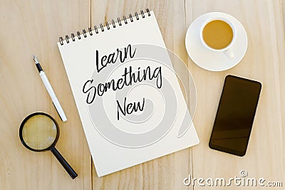 Top view of a cup of coffee,mobile phone,pen and notebook written with Learning Something New on wooden background. Business and Stock Photo