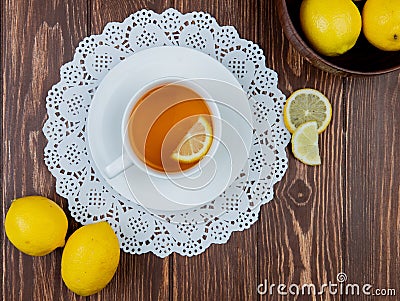 top view of cup of tea with lemon slice in it on paper doily and lemons on wooden background Stock Photo