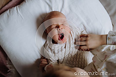 Top view of cute little baby yawning in bed, big sister holding newborn hand. Sisterly love, joy for new family member. Stock Photo