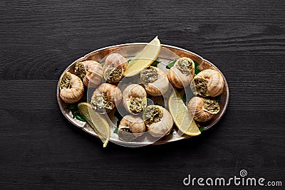 Top view of delicious cooked escargots with lemon on black wooden table. Stock Photo