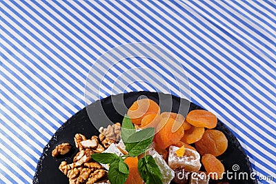 Top view of a desert. Dry apricots, walnuts and mint on a plate of turkish delight on a striped background. Copy space. Stock Photo