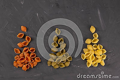 Top view of dry conchiglie pasta on black board background. Three triangular slides with pasta conchiglie spread out in colors, Stock Photo