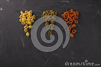 Top view of dry conchiglie pasta on black board background. Three triangular slides with pasta conchiglie spread out in colors, Stock Photo