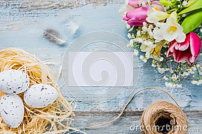 Top view of easter eggs in a nest. Spring flowers and feathers over blue rustic wood background. Empty card. Stock Photo