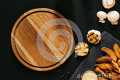 top view of empty wooden board, grilled garlic, mushrooms and baked potatoes with sauce Stock Photo