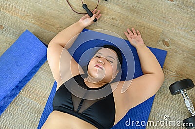 Top view of exhausted overweight Asian woman lying on yoga mat after training in gym. Young chubby woman hard work to lose weight Stock Photo
