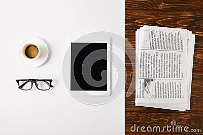 top view of eyeglasses, coffee cup, and digital tablet with blank screen on white and pile of newspapers on wooden background Stock Photo