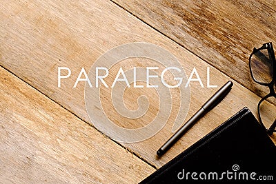 Top view of eyeglasses,notebook and pen on wooden background written with PARALEGAL Stock Photo