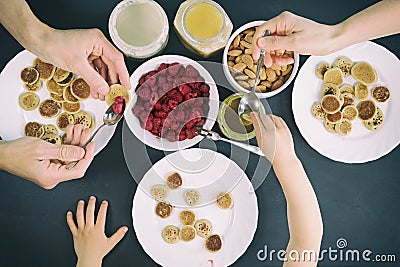 Top view family eating homemade breakfast. Tiny mini pancake cereal, sweet spreads, nuts, honey and fresh raspberries. Parents and Stock Photo