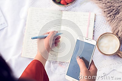 Top view of female hands with a phone and a pen, writting something in a sketchbook Stock Photo