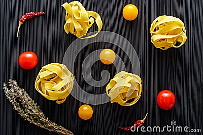 Top view fettuccine with yellow and red tomatoes, chili, sprig of thyme on background of black spaghetti with cuttlefish ink Stock Photo
