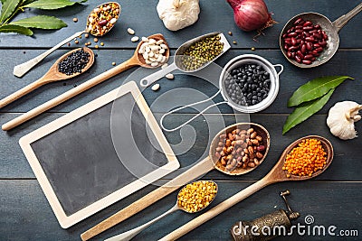 Top view of flat lay of assortment of legumes on black wooden tabletop, in scoop and ladles and a small blackboard Stock Photo