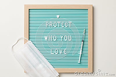 Top view of a frame with protect who you love writen, a white surgical mask and a syringe shot or vaccine Stock Photo