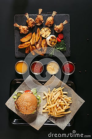 top view of french fries with delicious burger on tray, assorted sauces and slate board with roasted potatoes, grilled vegetables Stock Photo