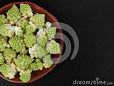 top view of fresh romanesco florets in wooden bowl on black slate plate with copy space Stock Photo