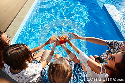 Top view of of friends clinking glasses with fresh colorful cocktails sitting by swimming pool on sunny summer day Stock Photo