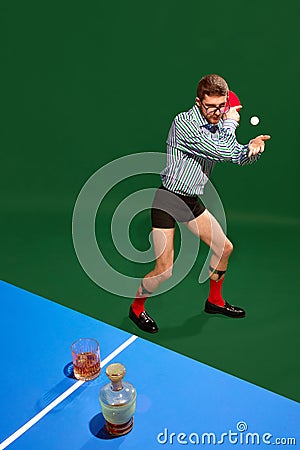 Top view. Funny creative photo with man un shirt and underweared playing table tennis with whiskey glass over green Stock Photo