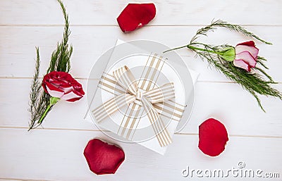 top view of a gift box tied with bow and red color roses with scattered petals and asparagus on white wooden background Stock Photo