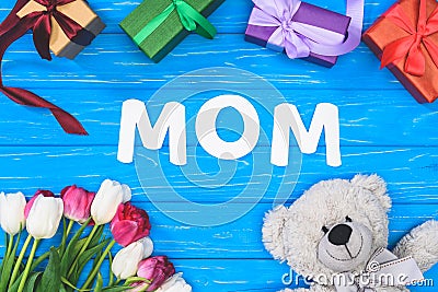 top view of gift boxes, teddy bear, tulips and word mom on blue table, mothers day concept Stock Photo